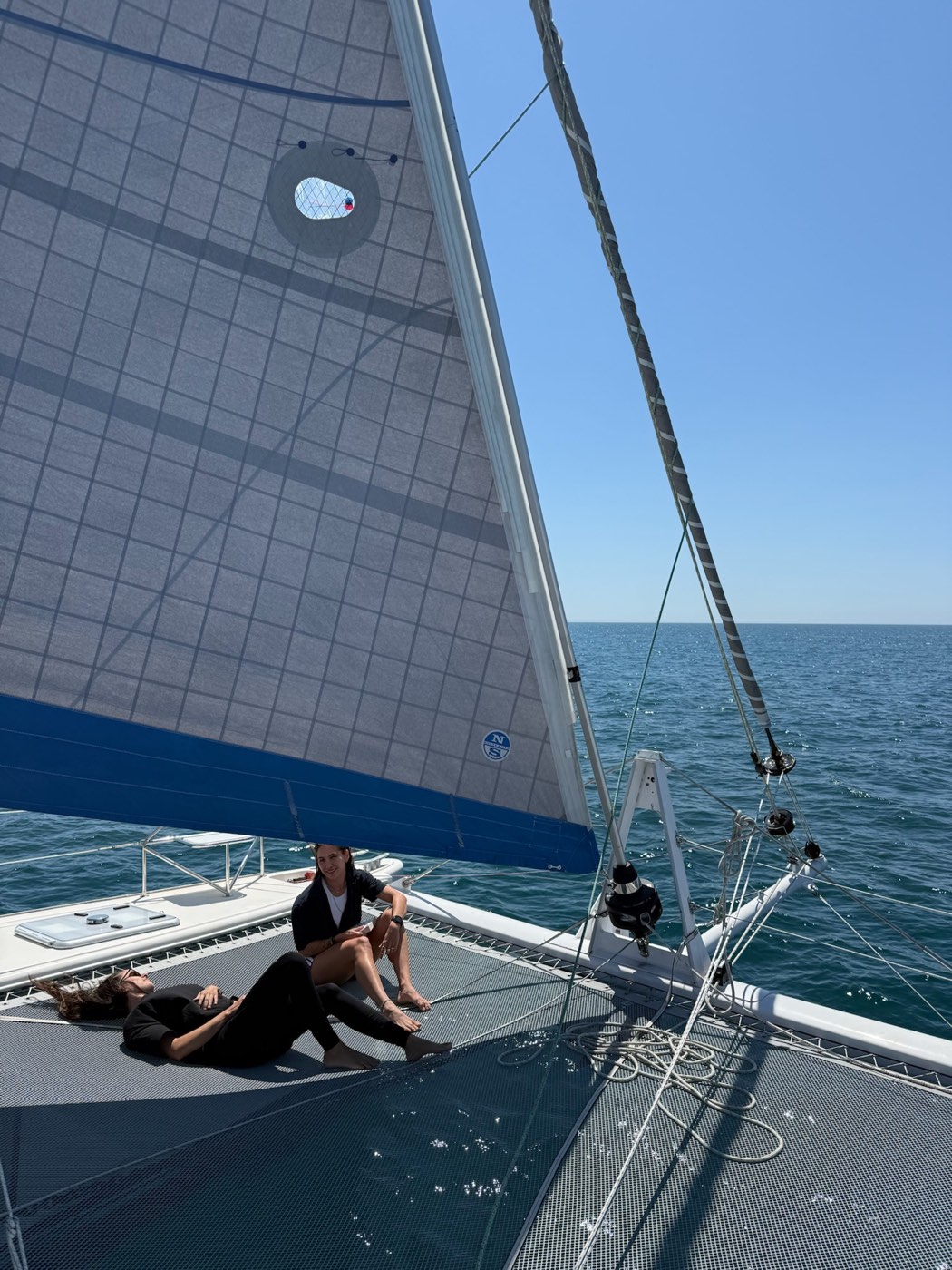 Guests relaxing on the trampoline of Little Cloud, our Catana 431 catamaran, under full sail