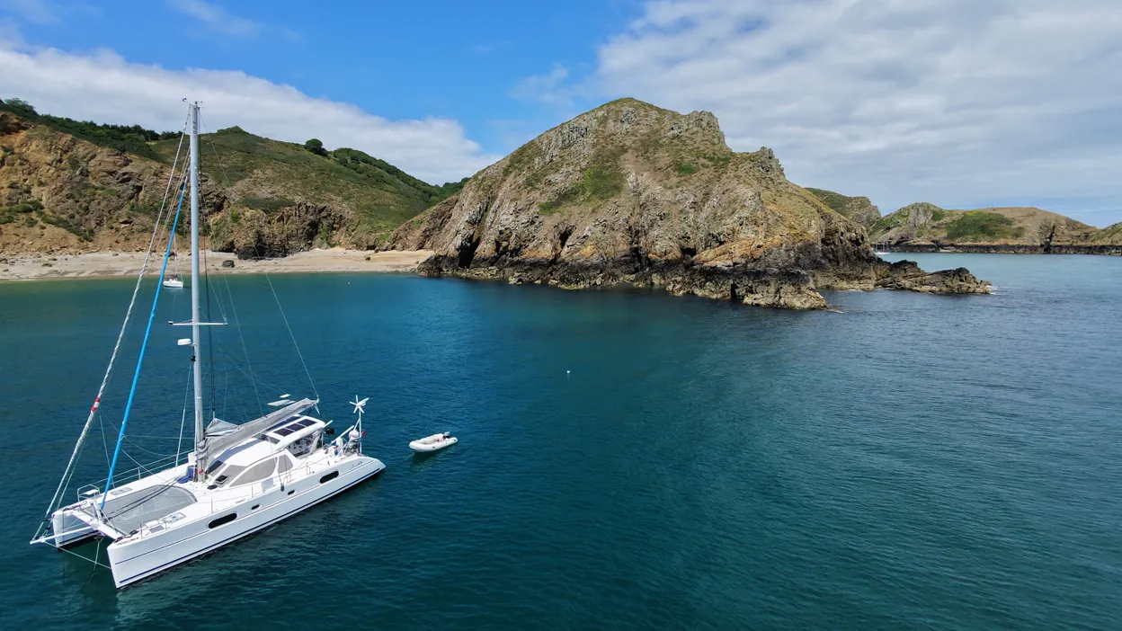 Little Cloud, our Catana 431 sailing catamaran, anchored beneath the headland of a wild bay in Sark, Channel Islands